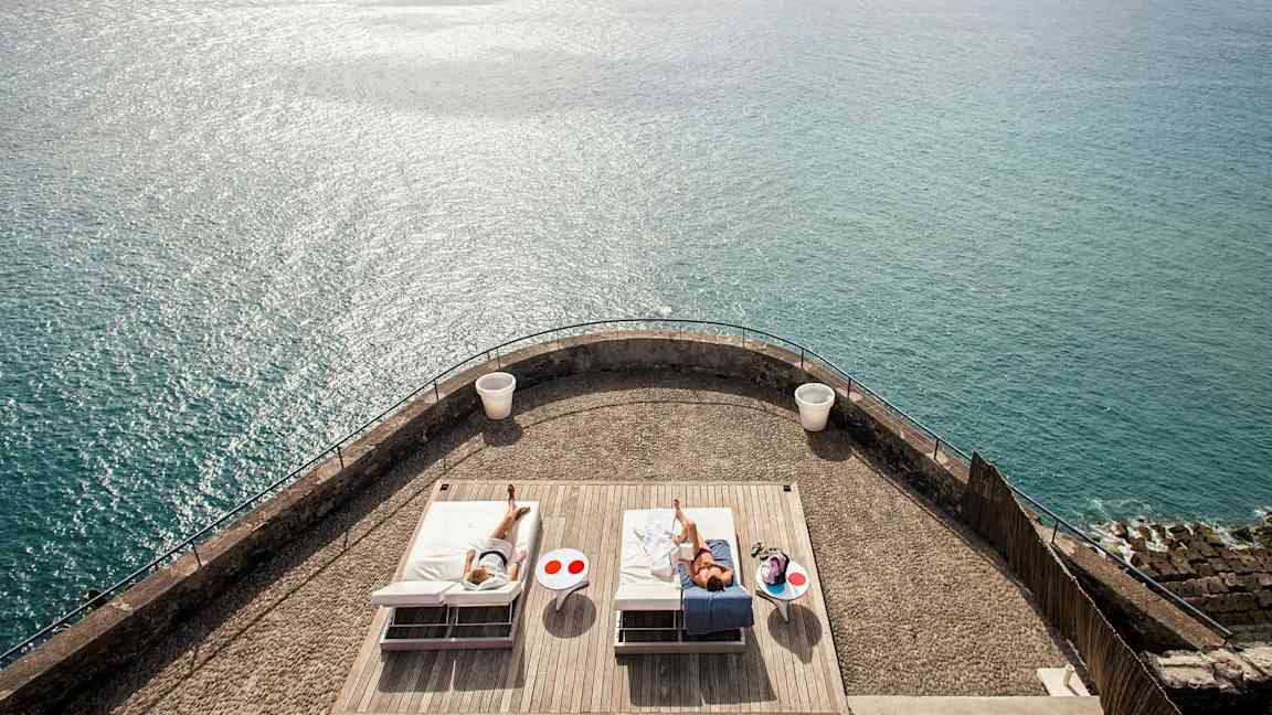 En terrasse med to solsenge og havet i baggrunden. (AI-genereret tekst)