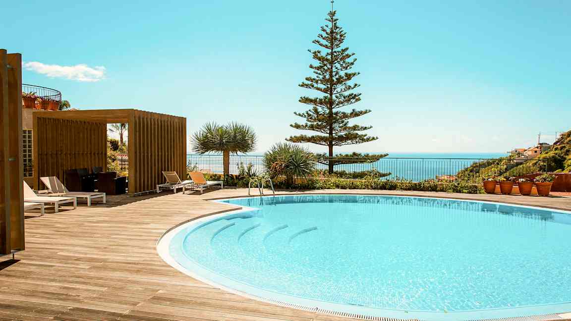 Udendørs swimmingpool omgivet af træterrasse og liggestole med udsigt over havet. (AI-genereret tekst)