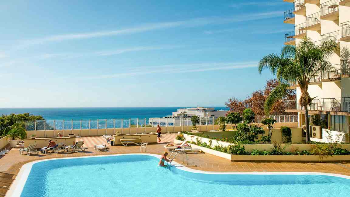 En udendørs swimmingpool med liggestole og en klar blå himmel over havet. (AI-genereret tekst)