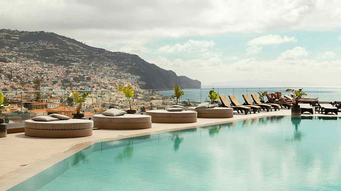 En infinitypool med liggestole og udsigt over en by og bjerge. (AI-genereret tekst)