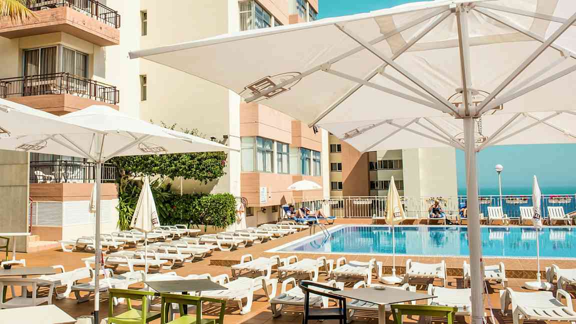 Udendørs poolområde med liggestole og parasoller ved et hotel. (AI-genereret tekst)