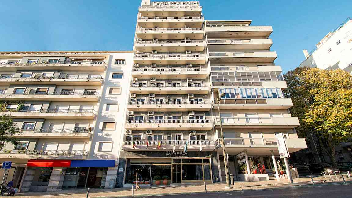Lejlighedsbygning med hotelskilt og altaner under en klar blå himmel. (AI-genereret tekst)