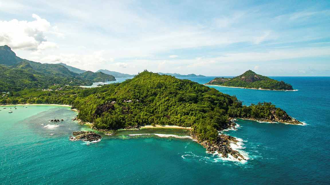 Luftfoto af en frodig ø omgivet af klart blåt hav og mindre øer i baggrunden. (AI-genereret tekst)