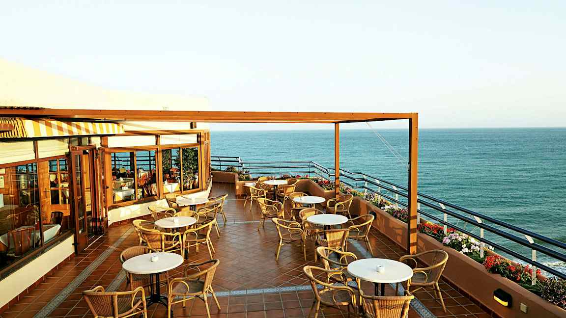 En terrasse med borde og stole og udsigt over havet. (AI-genereret tekst)