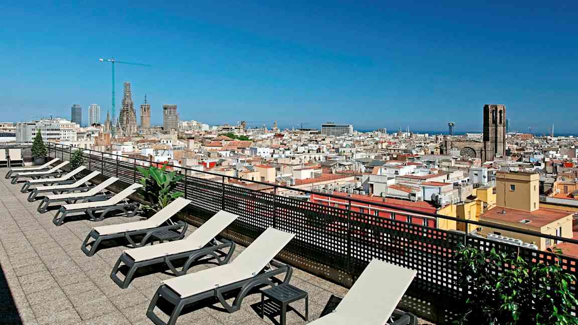 En tagterrasse med liggestole og udsigt over en by med kirke og blå himmel. (AI-genereret tekst)