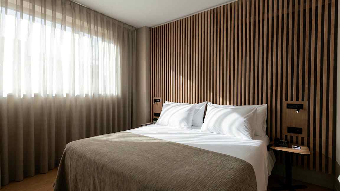 En seng i et moderne soveværelse med træpanel og lysindfald fra et vindue. (AI-genereret tekst)