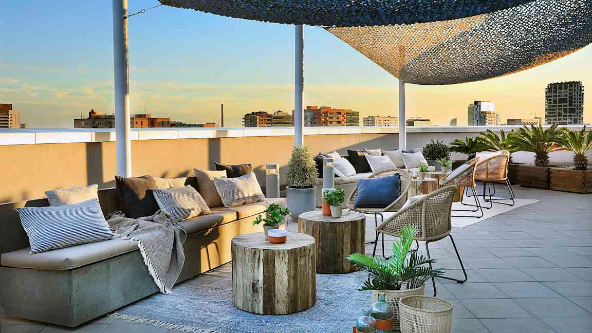 En tagterrasse med siddepladser, borde og kurve dekoreret med planter og puder er afbildet. (AI-genereret tekst)