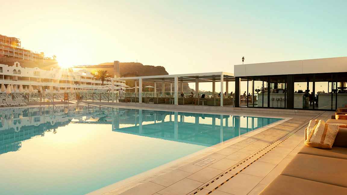 Udendørs swimmingpool ved et hotel med liggestole og en bygning i baggrunden. (AI-genereret tekst)