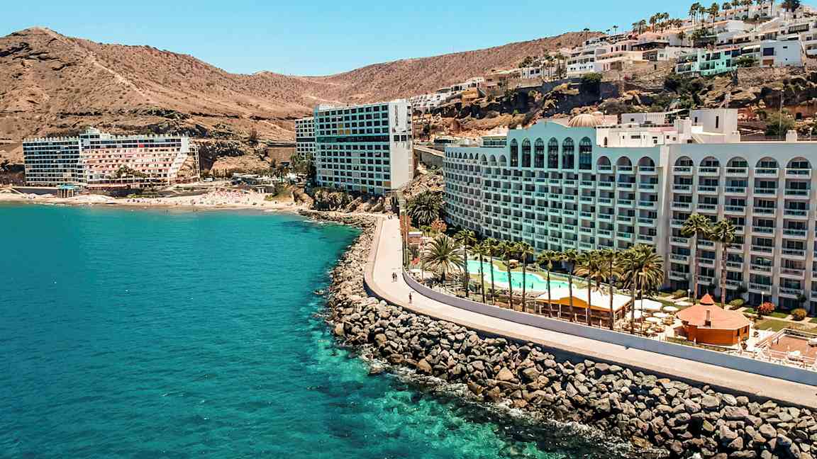 Hotel ved en kyst med klipper, pool og palmer. (AI-genereret tekst)