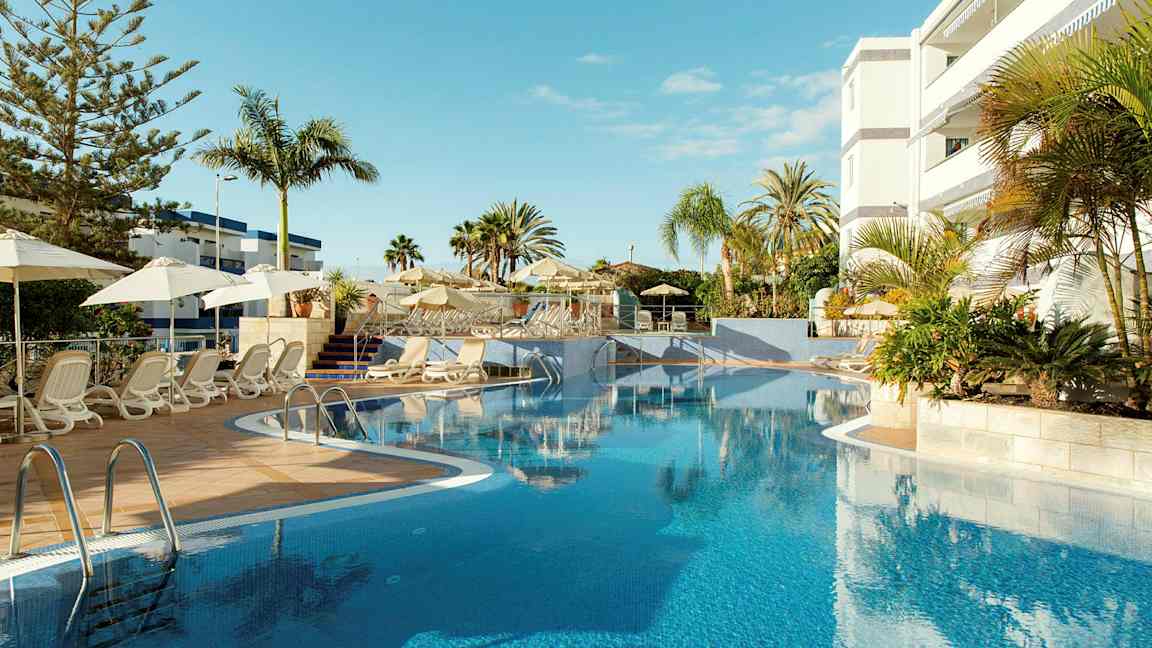 Udendørs pool med liggestole og parasoller ved et hotel. (AI-genereret tekst)