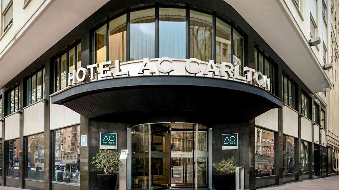 En hotelfacade med skilteteksten "HOTEL AC CARLTON" synlig over indgangen. (AI-genereret tekst)