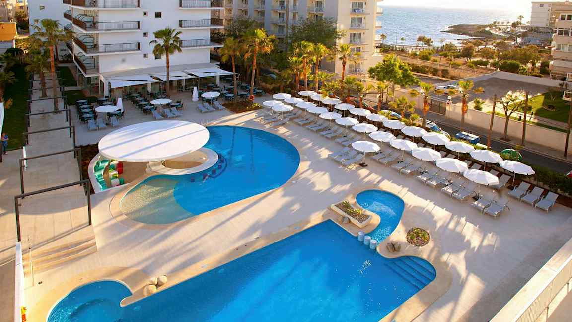 Hotelområde nær havet med pool, liggestole og parasoller. (AI-genereret tekst)
