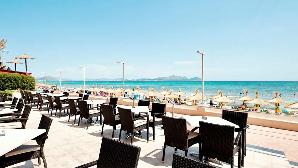 Udendørs servering med udsigt til en sandstrand og havet med parasoller. (AI-genereret tekst)