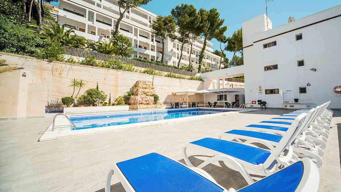 Liggestole ved en pool med hotelbygning i baggrunden. (AI-genereret tekst)