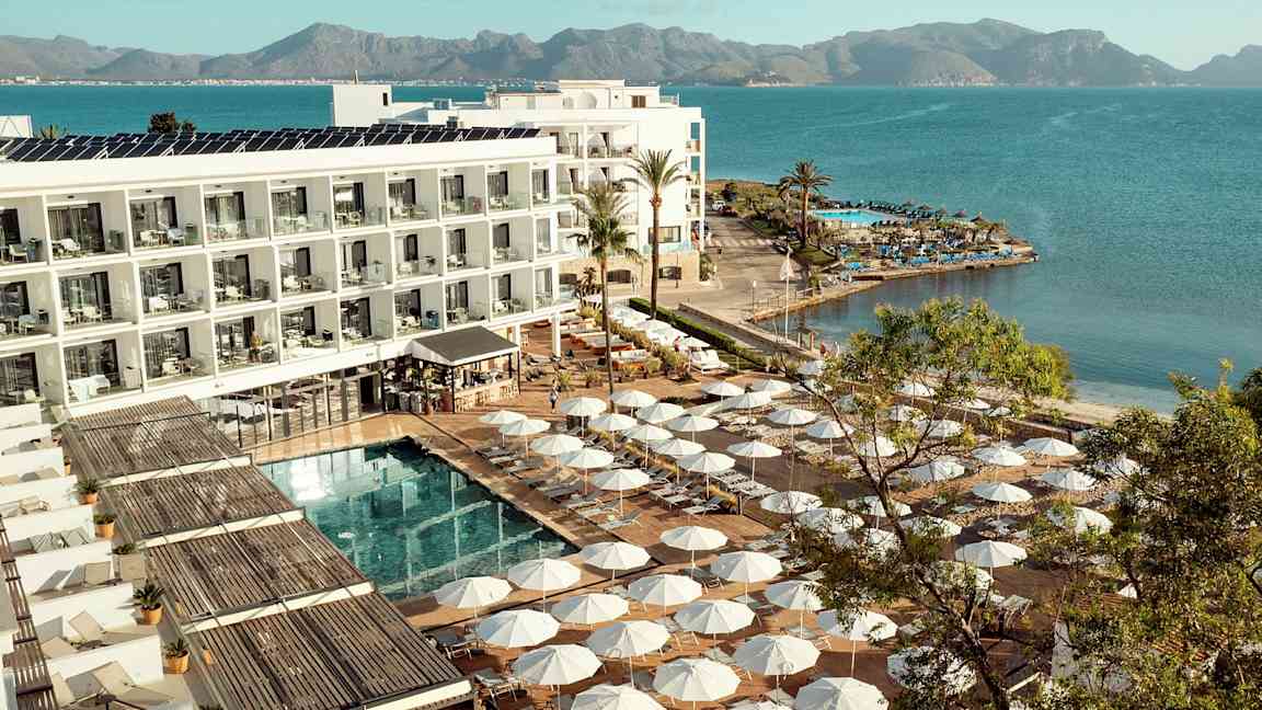 Hotelkompleks ved vandkanten med solsenge og parasoller omkring en pool. (AI-genereret tekst)