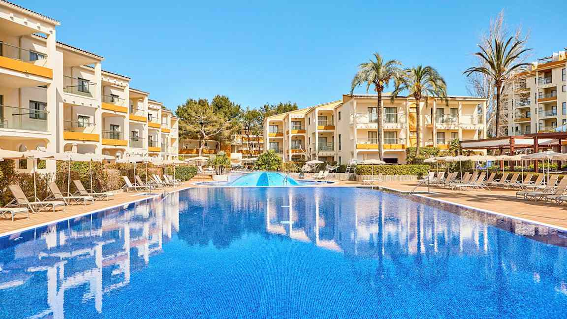 Billede af en udendørs pool med bygninger og liggestole i baggrunden. (AI-genereret tekst)