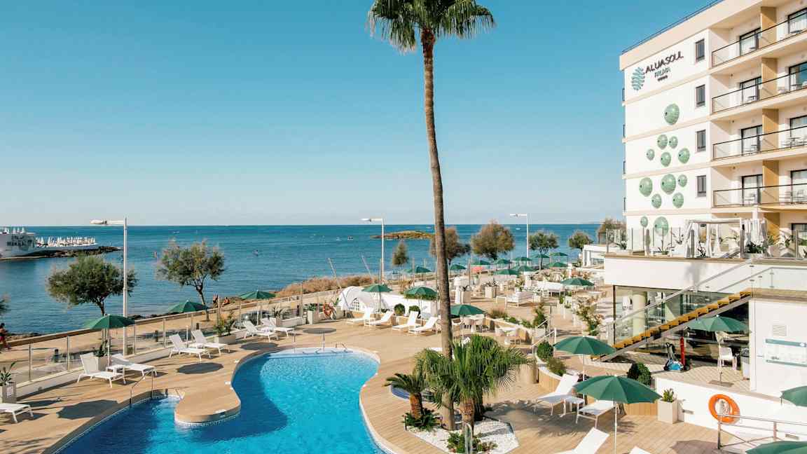 En udendørs pool ved et hotel nær havet med liggestole og parasoller på en træterrasse. (AI-genereret tekst)