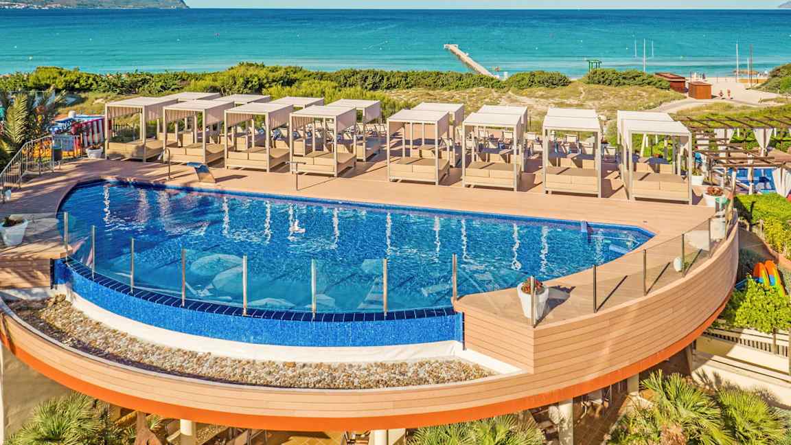 Udendørs pool med solsenge på en træterrasse tæt på stranden. (AI-genereret tekst)