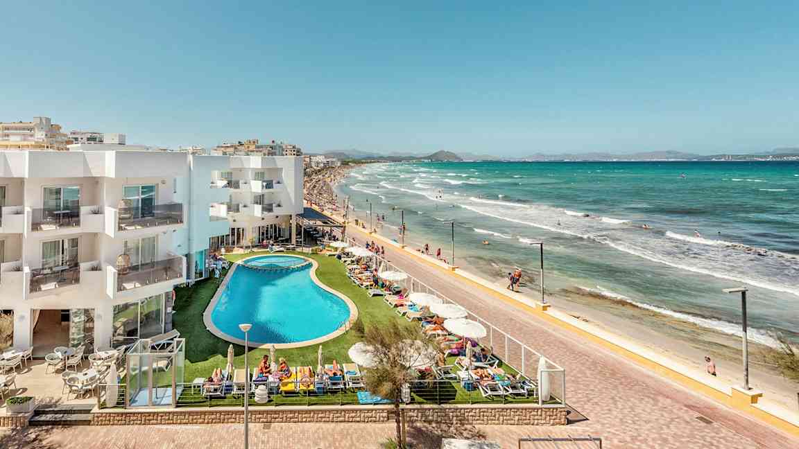 Hotelbygning og poolområde ved strandpromenade og sandstrand. (AI-genereret tekst)