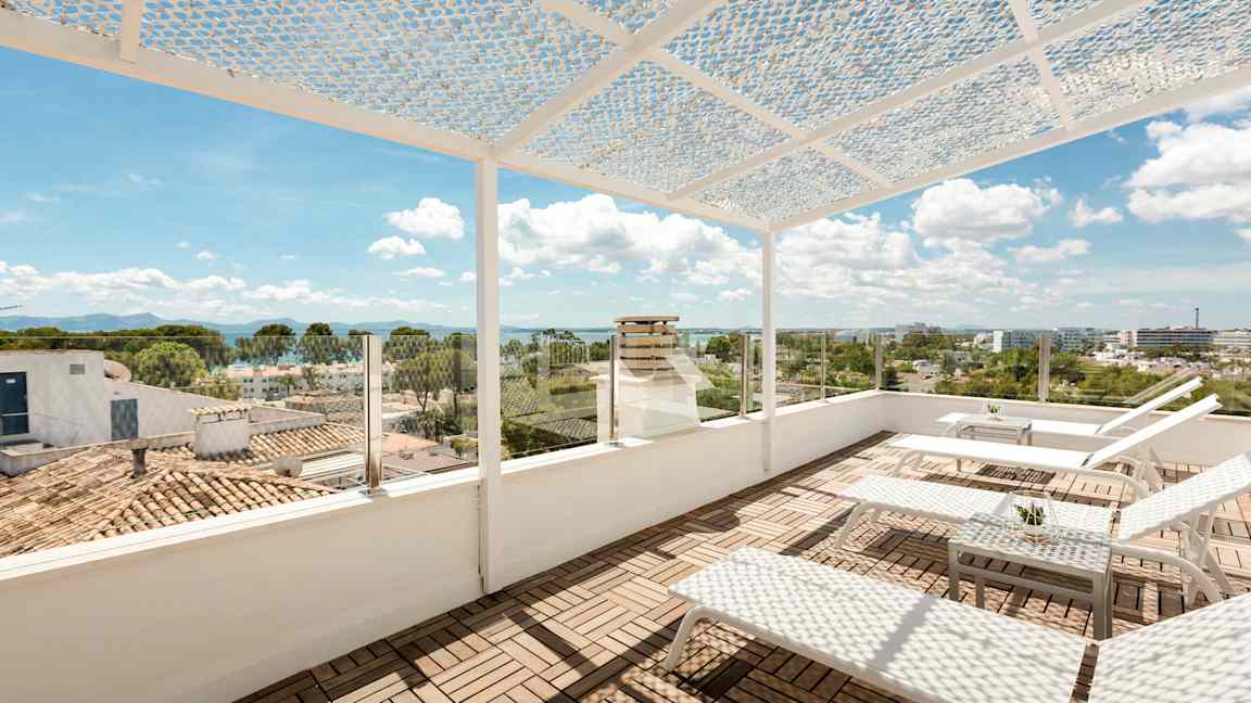 En tagterrasse med liggestole og et bord. Terrassen har et perforeret overdække og glasværn med udsigt over byen og havet. (AI-genereret tekst)