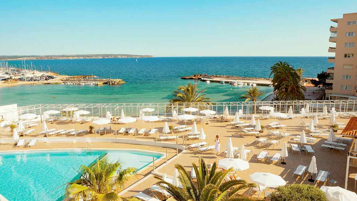 Poolområde med liggestole og parasoller tæt på havet. (AI-genereret tekst)