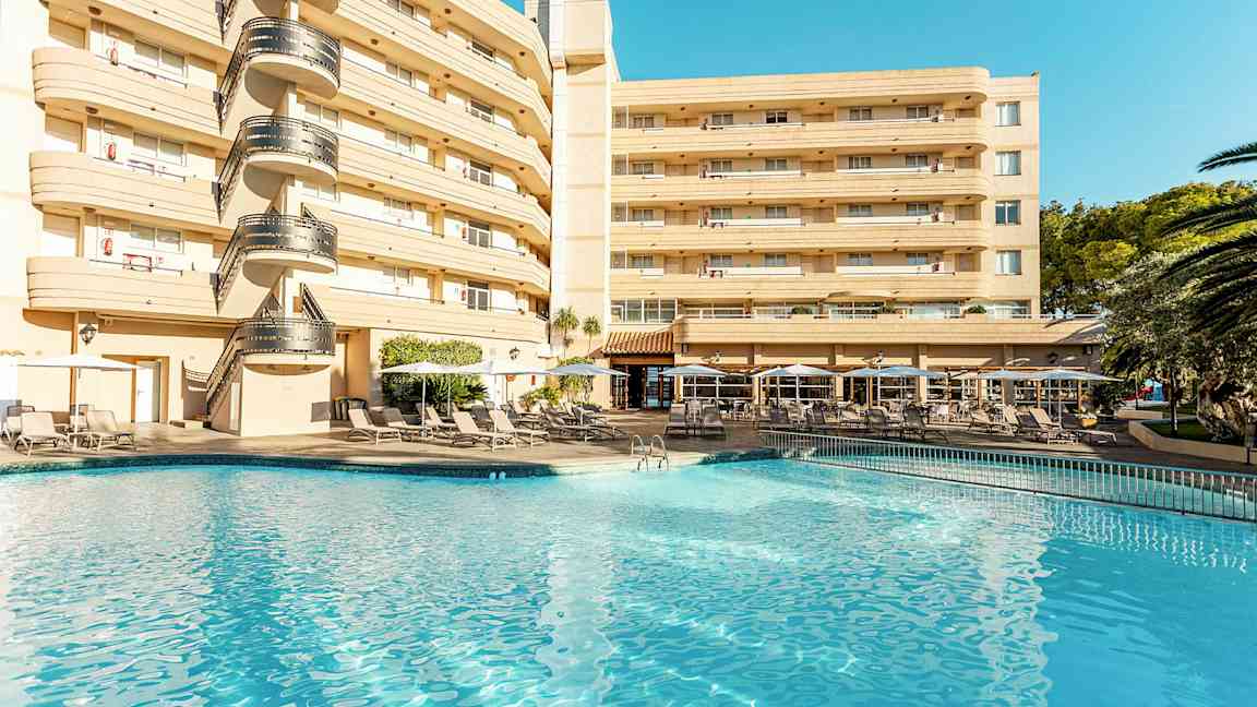 Hotelbygning ved en pool med liggestole og parasoller. (AI-genereret tekst)