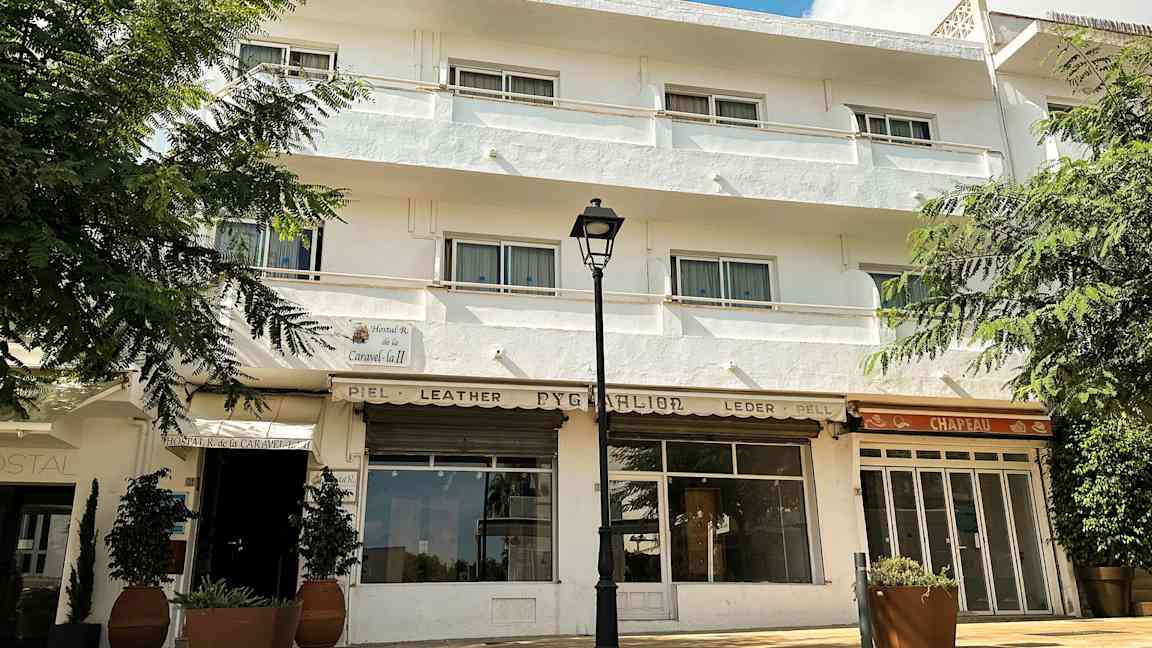 Hvid bygning med flere vinduer og altaner, omgivet af grønne områder. (AI-genereret tekst)