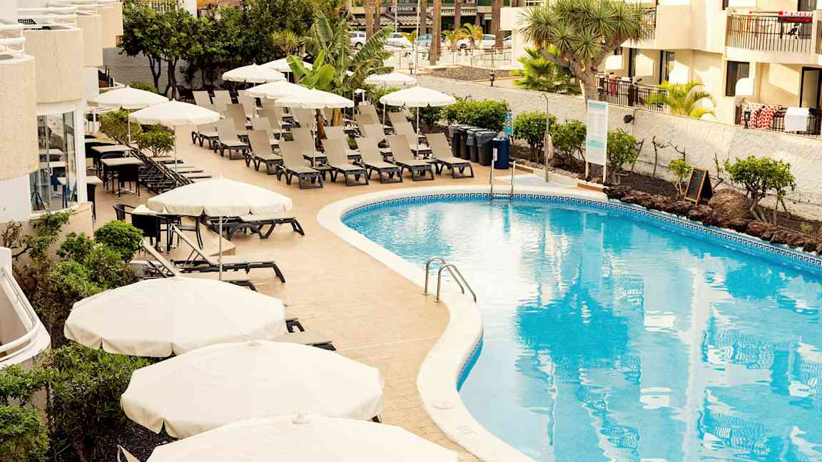 Poolområde med liggestole og parasoller ved et hotel. (AI-genereret tekst)