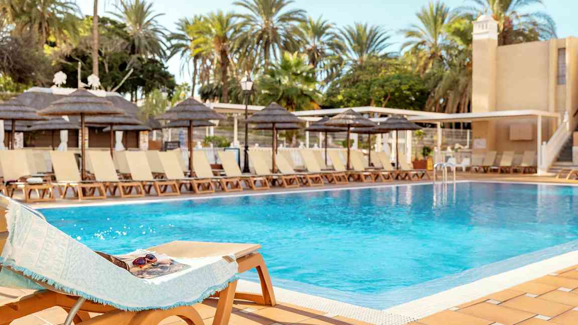 En pool omgivet af liggestole og palmer under en klar himmel. (AI-genereret tekst)