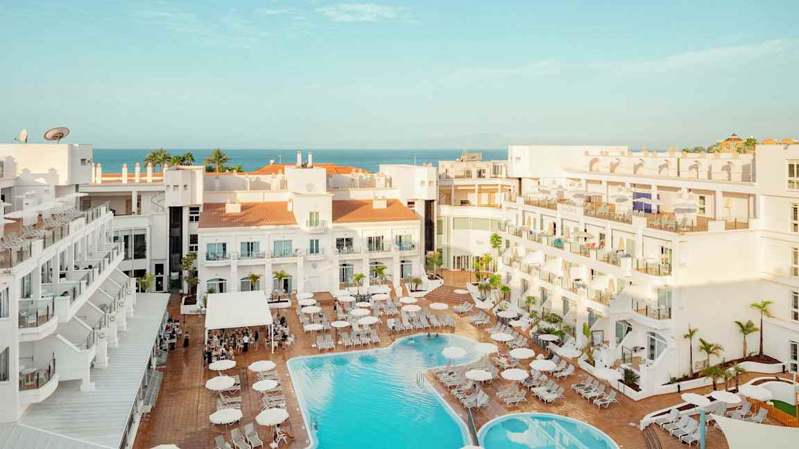 Udsigt over hotelområde med pool og liggestole, havet kan ses i baggrunden. (AI-genereret tekst)