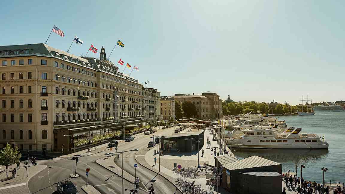 Udsigt over en by med en gade, bygninger med flag og både ved en kaj. (AI-genereret tekst)