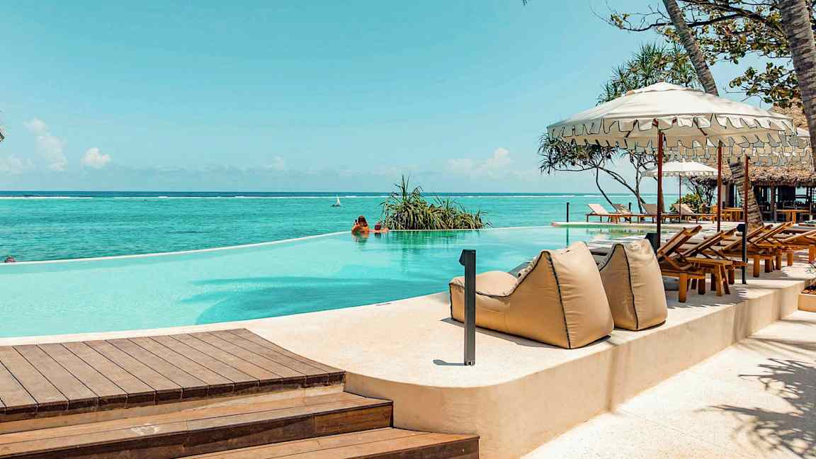 En infinity-pool ved havet, omgivet af liggestole og parasoller. (AI-genereret tekst)