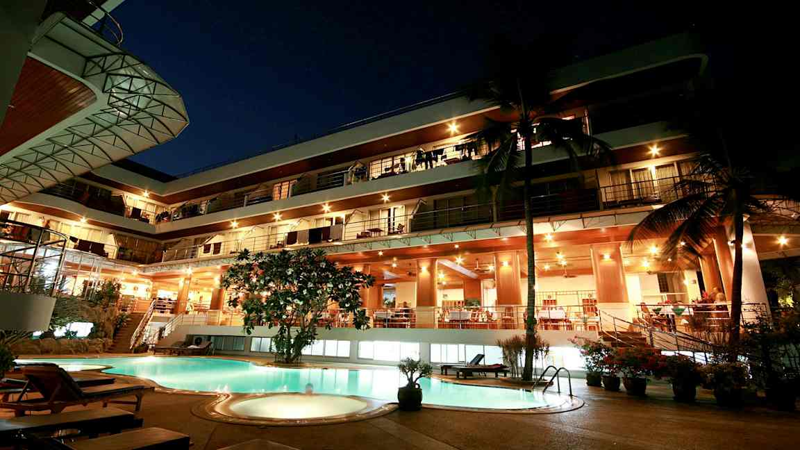 Aftenudsigt af en fleretagers bygning med oplyst facade og en pool i forgrunden. (AI-genereret tekst)