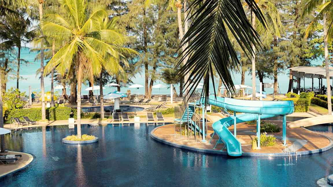 En udendørs pool med en blå vandrutsjebane og palmer omkring. (AI-genereret tekst)