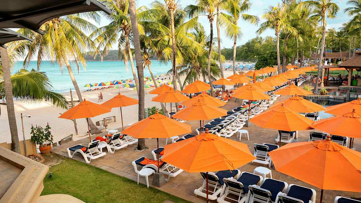 Liggestole og orange parasoller ved en strand med palmer. (AI-genereret tekst)
