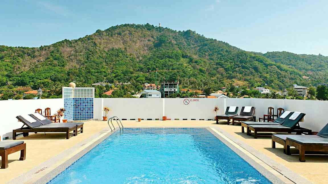 Udendørs pool med liggestole og bjerge i baggrunden. (AI-genereret tekst)