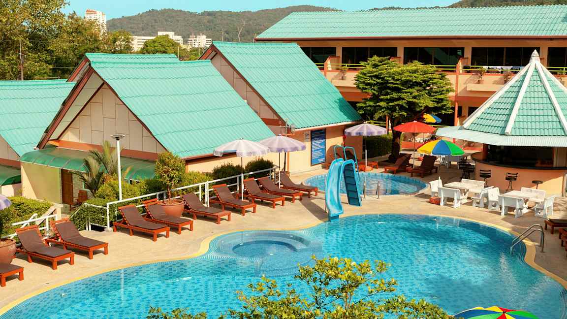 Udendørs poolområde med liggestole, parasoller og bygninger med grønne tage. (AI-genereret tekst)