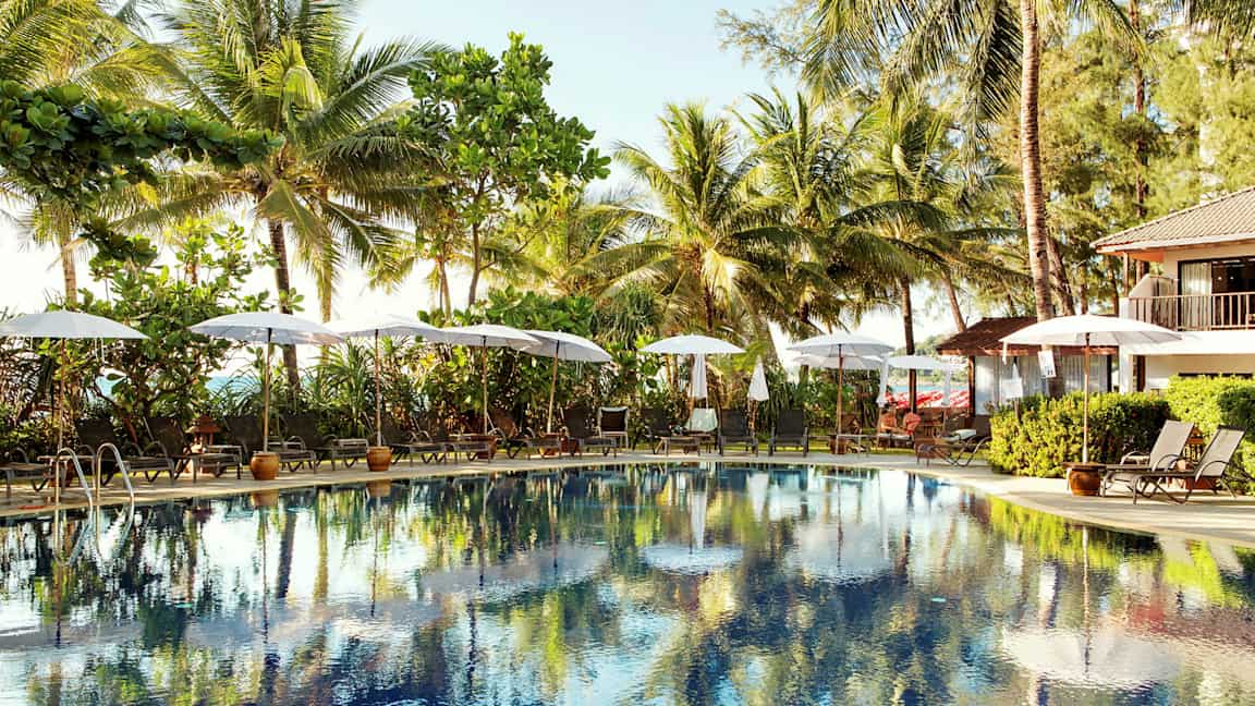 Udendørs pool omgivet af liggestole og parasoller, med palmer i baggrunden. (AI-genereret tekst)