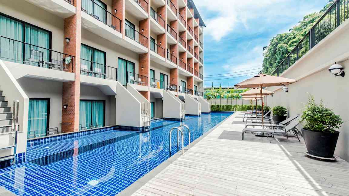 Et hotel med flere etager og en lang pool foran bygningen, omgivet af liggestole og parasoller. (AI-genereret tekst)