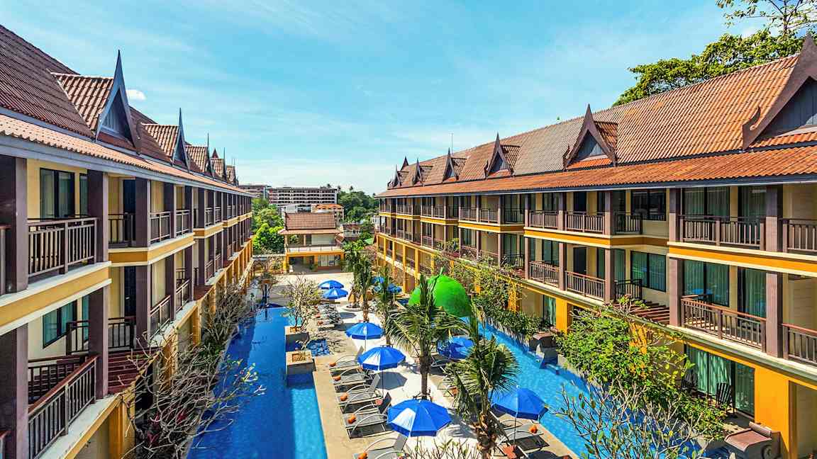 Toetagers hotelbygninger med skrånende tage omgiver en pool med liggestole og parasoller. (AI-genereret tekst)