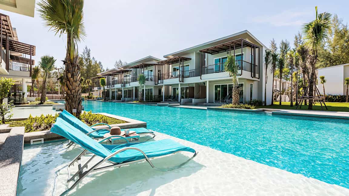 Billede af liggestole ved en pool foran moderne ferieboliger. (AI-genereret tekst)