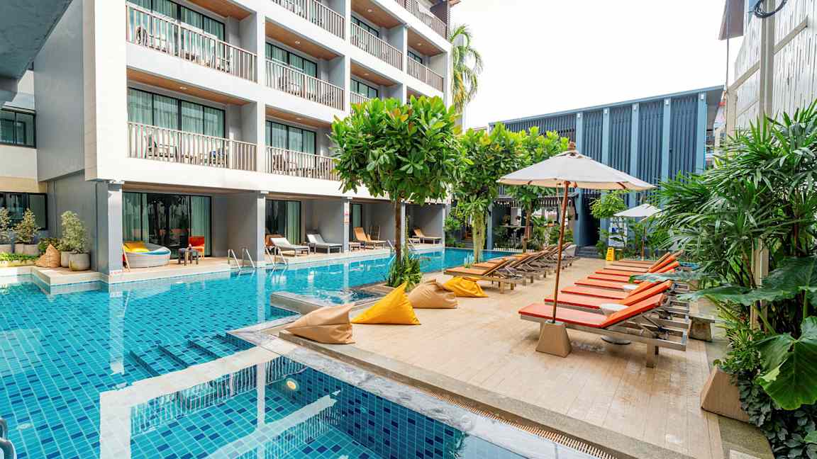 En moderne hotelbygning ved siden af en pool med liggestole og parasoller. (AI-genereret tekst)