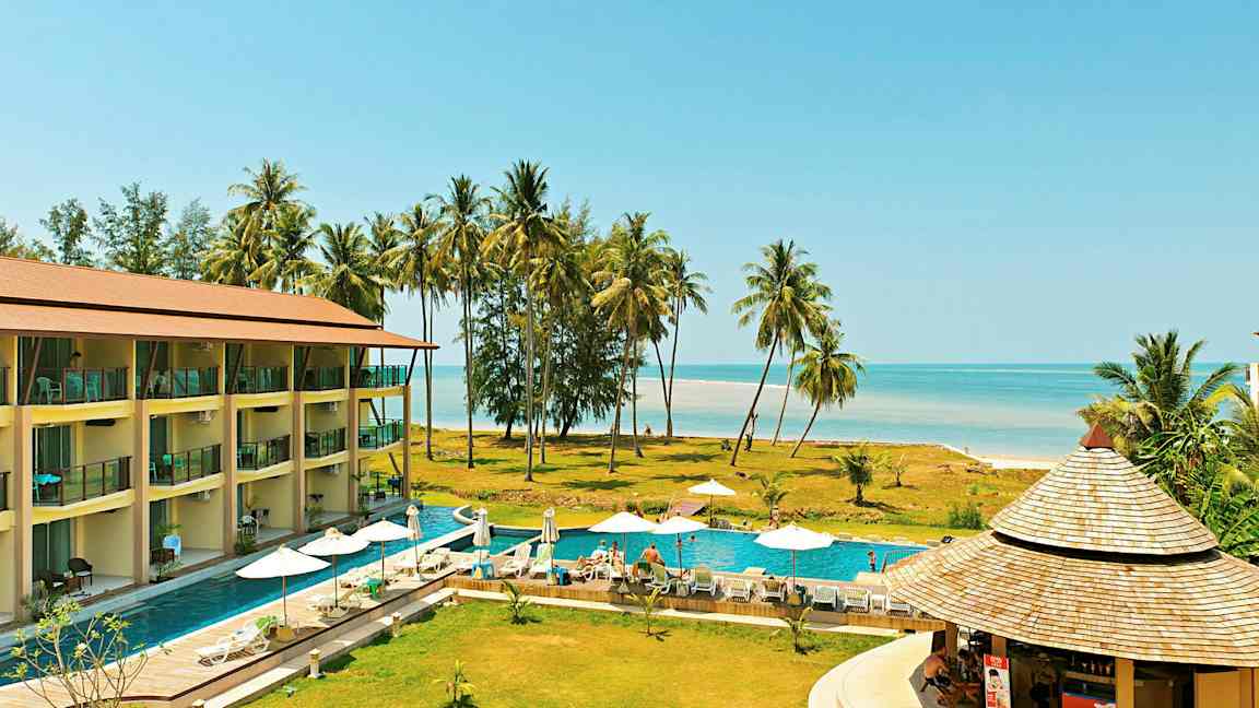 Et feriested med en pool, liggestole og parasoller, tæt på stranden med palmer. (AI-genereret tekst)