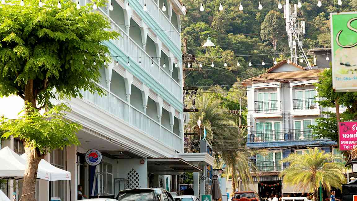 Gadebillede med parkerede biler, en bygning med blå facade og frodige træer. (AI-genereret tekst)