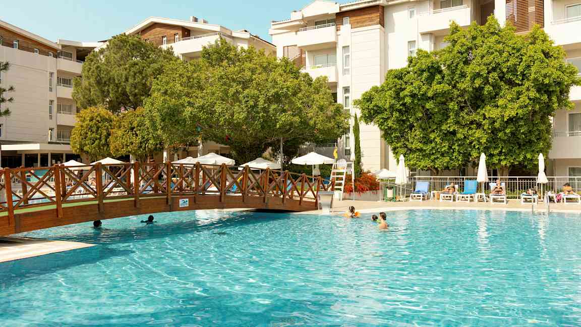 Udendørs pool med liggestole og træer i baggrunden. (AI-genereret tekst)