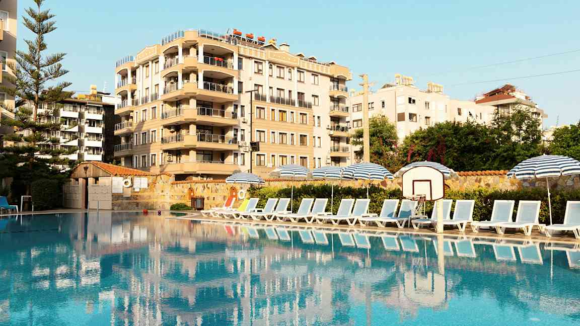 Billede af en pool med solsenge og parasoller ved siden af, samt en bygning i baggrunden. (AI-genereret tekst)