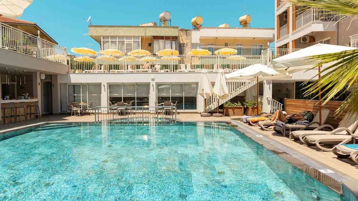En udendørs pool omgivet af liggestole og parasoller på et hotel. (AI-genereret tekst)