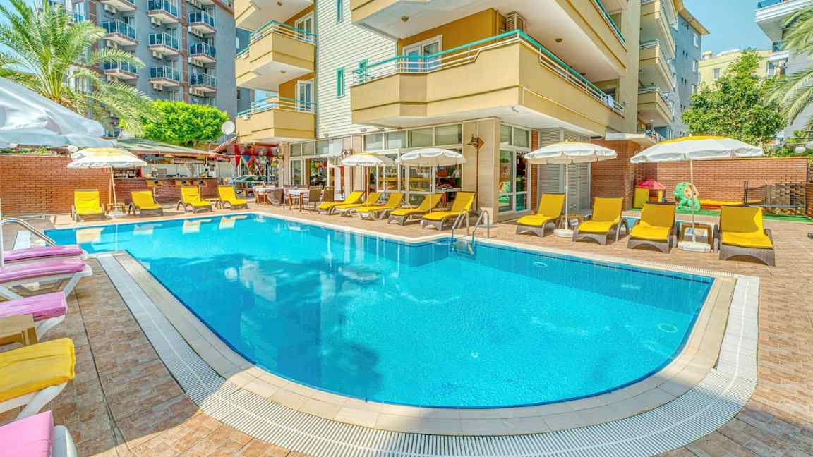 En udendørs pool omgivet af solsenge og parasoller foran en hotelbygning. (AI-genereret tekst)