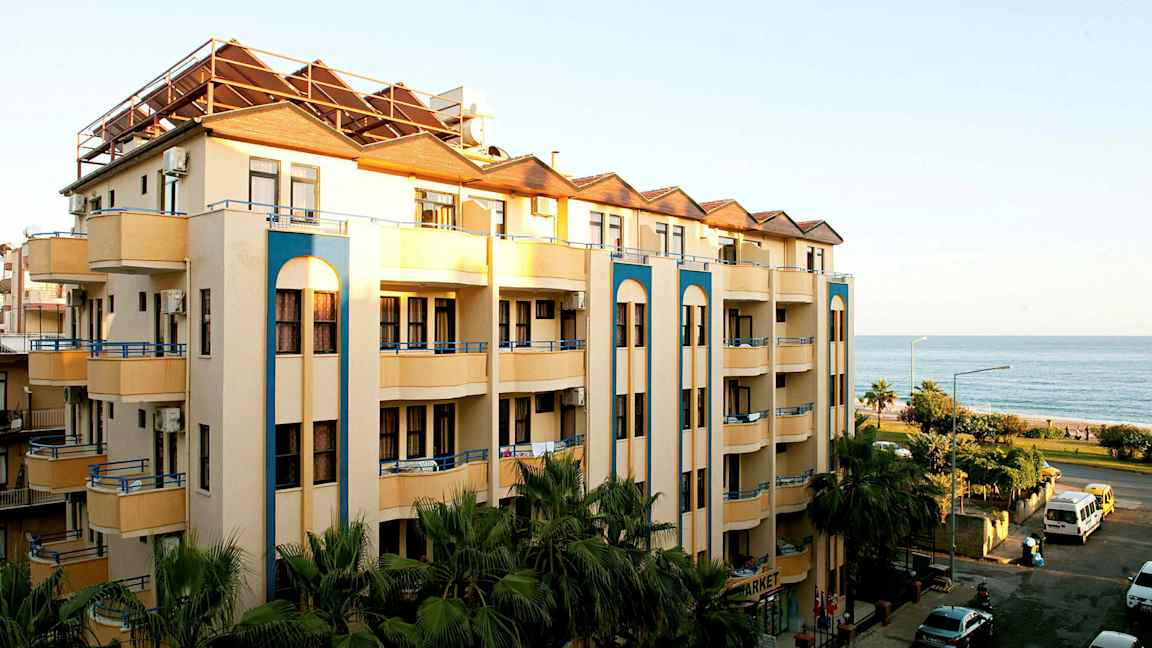 Billede af en fleretagers bygning med altaner tæt på havet. (AI-genereret tekst)