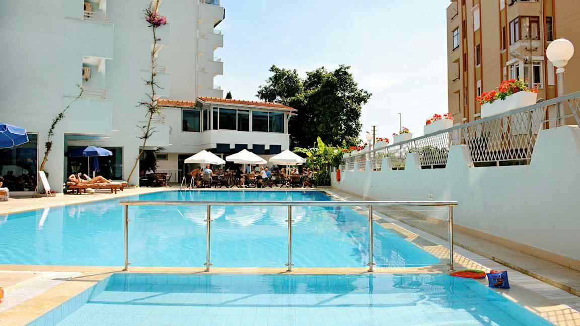 Et billede af et hotel med pool, siddeområde med parasoller og solsenge. (AI-genereret tekst)